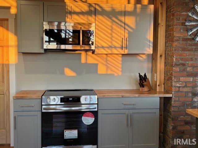 kitchen featuring butcher block counters, appliances with stainless steel finishes, and gray cabinetry