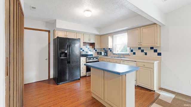 kitchen with backsplash, stainless steel electric stove, cream cabinetry, black fridge, and a sink