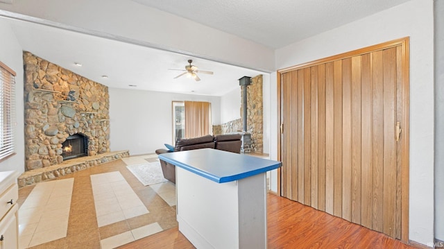 kitchen featuring ceiling fan, light wood finished floors, a textured ceiling, and a fireplace