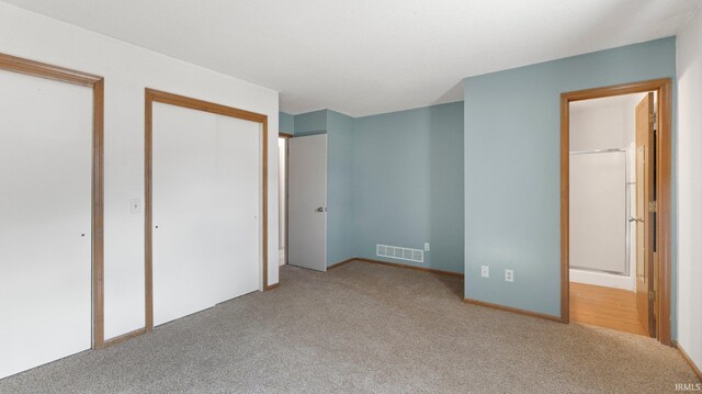 unfurnished bedroom with carpet, visible vents, and two closets