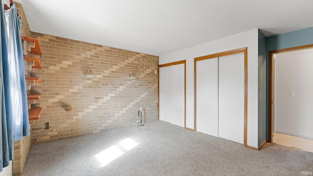 unfurnished bedroom featuring carpet floors, brick wall, and two closets