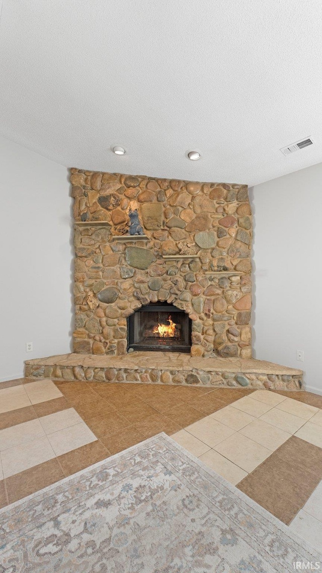 unfurnished living room featuring visible vents, a stone fireplace, a textured ceiling, and tile patterned floors