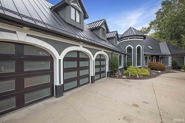 view of front facade with metal roof, driveway, a standing seam roof, and stucco siding