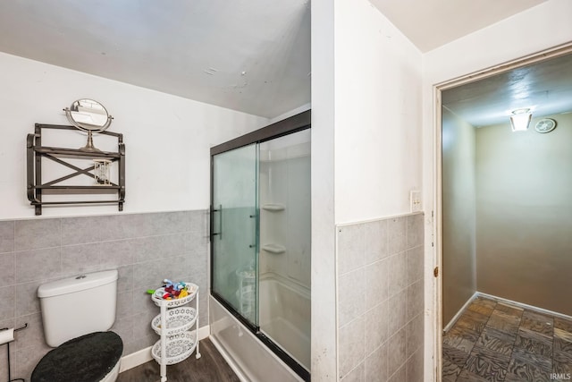 full bathroom featuring wainscoting, shower / bath combination with glass door, tile walls, and toilet