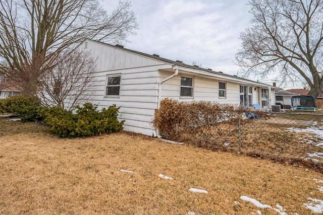 view of side of home featuring a trampoline, fence, and a yard