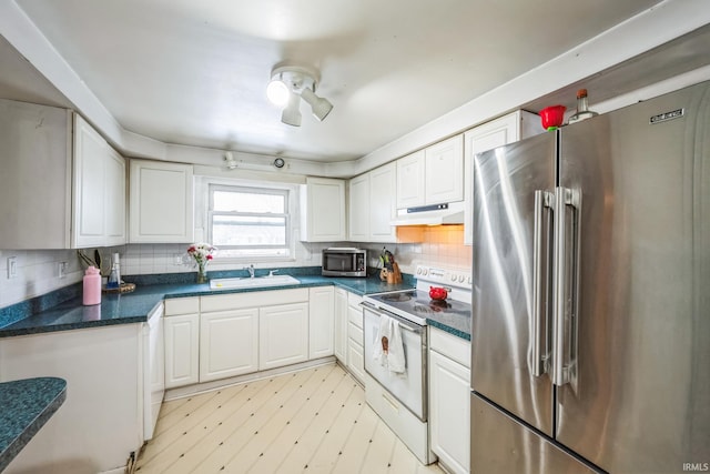 kitchen featuring stainless steel appliances, dark countertops, white cabinets, a sink, and under cabinet range hood