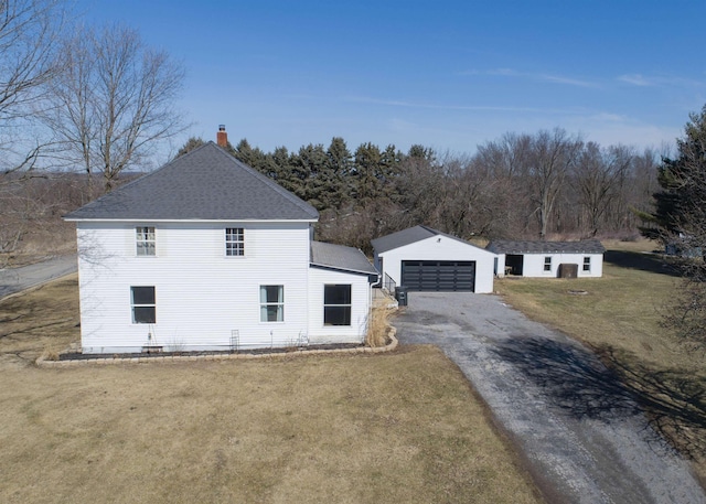 exterior space featuring a shingled roof, a chimney, a detached garage, an outdoor structure, and a front yard