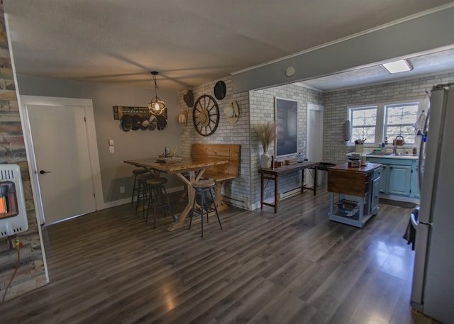 dining space with heating unit, dark wood-style floors, brick wall, and baseboards