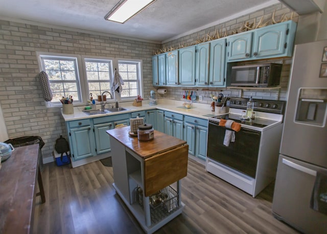 kitchen featuring brick wall, range with electric cooktop, a sink, refrigerator with ice dispenser, and stainless steel microwave