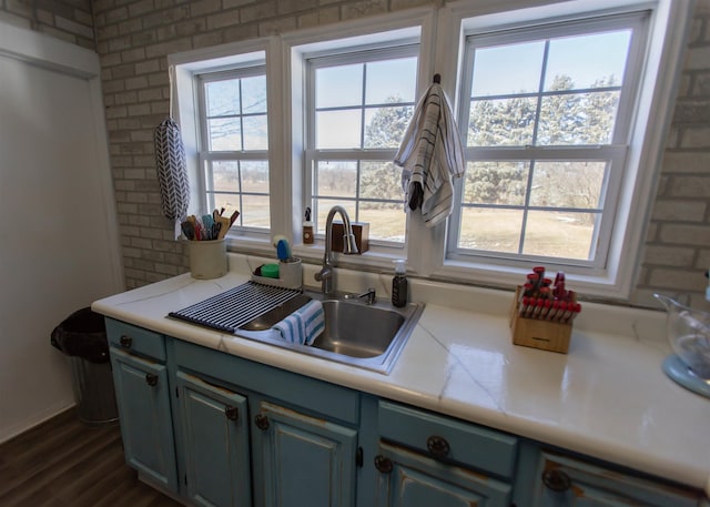 kitchen featuring dark wood-style floors, light countertops, a sink, and brick wall