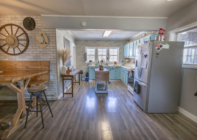 kitchen with blue cabinets, brick wall, light countertops, dark wood-style floors, and stainless steel fridge