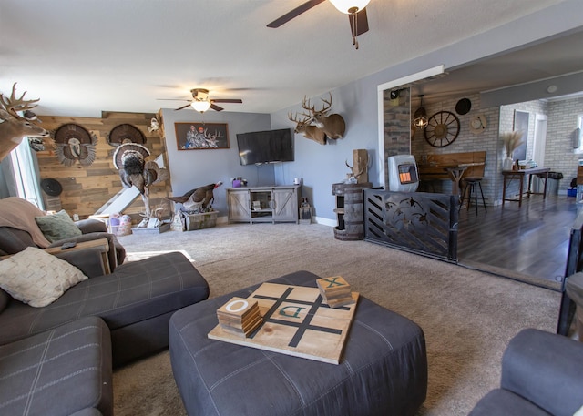 carpeted living area featuring baseboards, ceiling fan, an accent wall, wood walls, and a fireplace