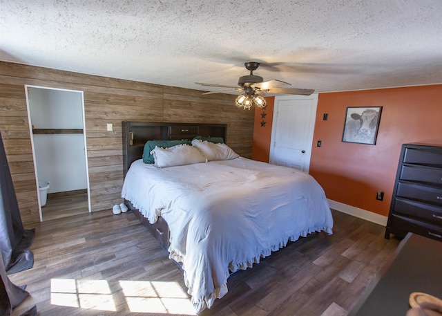 bedroom featuring wood walls, a textured ceiling, baseboards, and wood finished floors