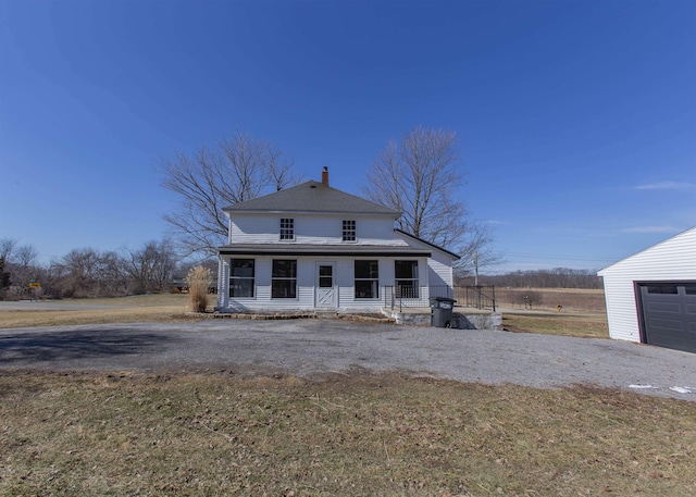 view of front facade featuring an outbuilding, driveway, a chimney, and a front yard