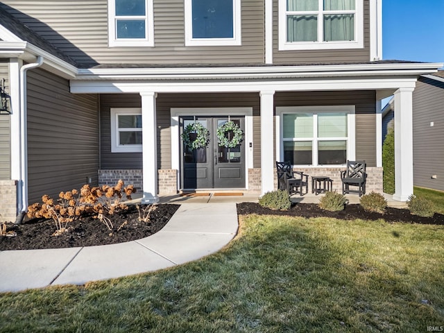 doorway to property with a porch, french doors, brick siding, and a lawn