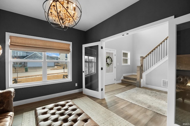 foyer entrance featuring wood finished floors, visible vents, baseboards, stairway, and an inviting chandelier