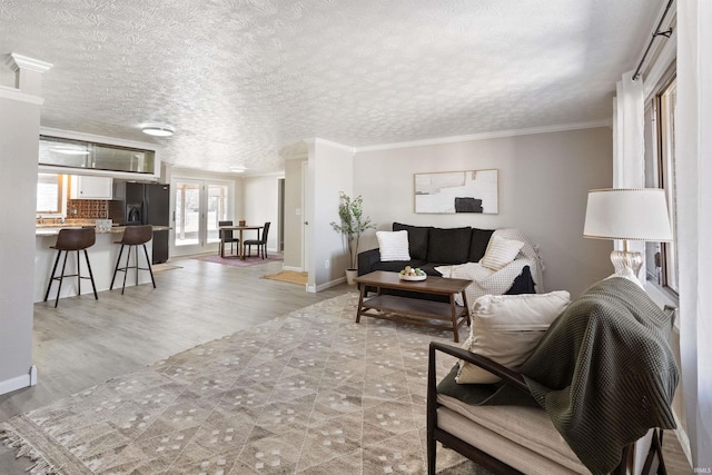 living room with light wood-style floors, baseboards, crown molding, and french doors