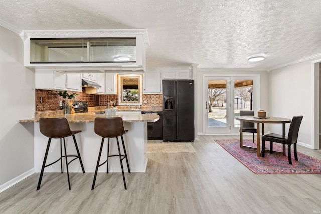 kitchen featuring under cabinet range hood, white cabinets, black fridge, and range with electric stovetop