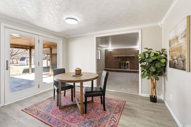 dining space featuring a fireplace, light wood finished floors, ornamental molding, a textured ceiling, and baseboards