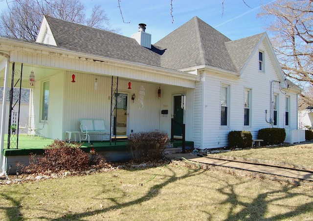 view of front of home with a chimney, central air condition unit, a shingled roof, covered porch, and a front yard