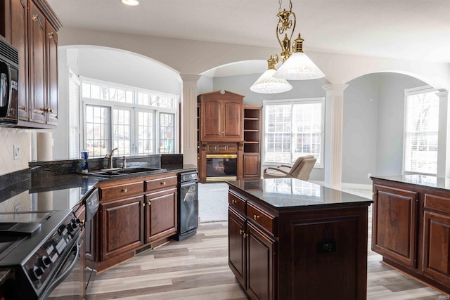 kitchen with light wood finished floors, dark stone counters, decorative light fixtures, black appliances, and a sink