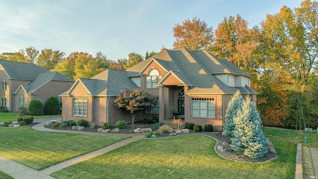 view of front of home featuring a shingled roof, a front yard, and brick siding