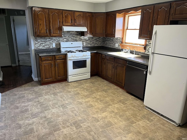 kitchen with dark countertops, backsplash, a sink, white appliances, and under cabinet range hood