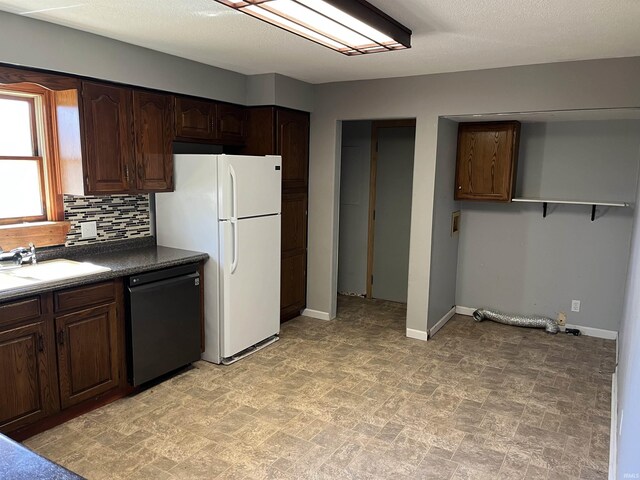 kitchen with dark brown cabinetry, a sink, black dishwasher, backsplash, and freestanding refrigerator