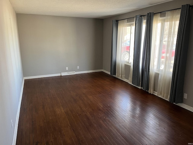 unfurnished room with dark wood-type flooring, visible vents, a textured ceiling, and baseboards