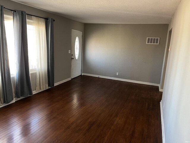 empty room featuring a textured ceiling, dark wood-style flooring, visible vents, and baseboards