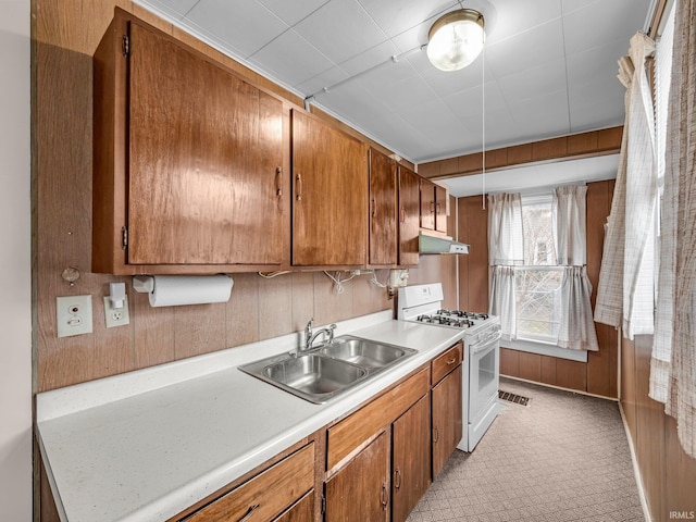 kitchen with under cabinet range hood, a sink, white gas range oven, brown cabinetry, and light countertops