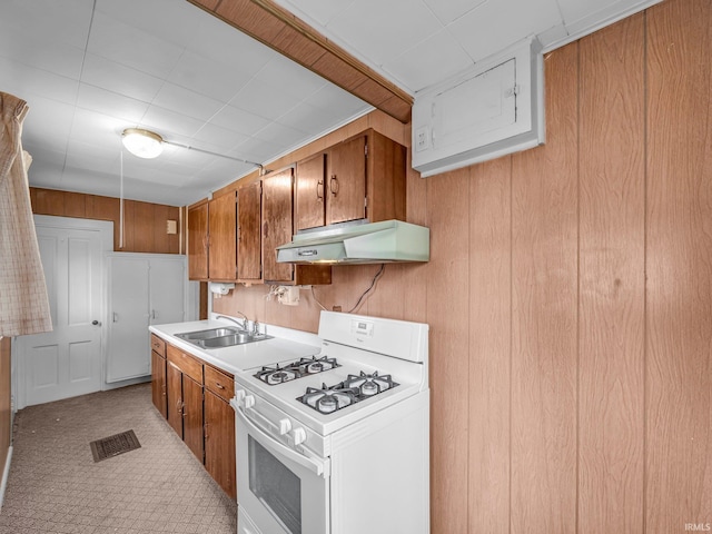 kitchen featuring visible vents, brown cabinets, under cabinet range hood, a sink, and white gas range oven