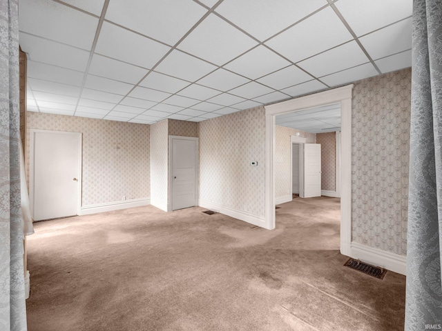 carpeted empty room with wallpapered walls, baseboards, visible vents, and a paneled ceiling