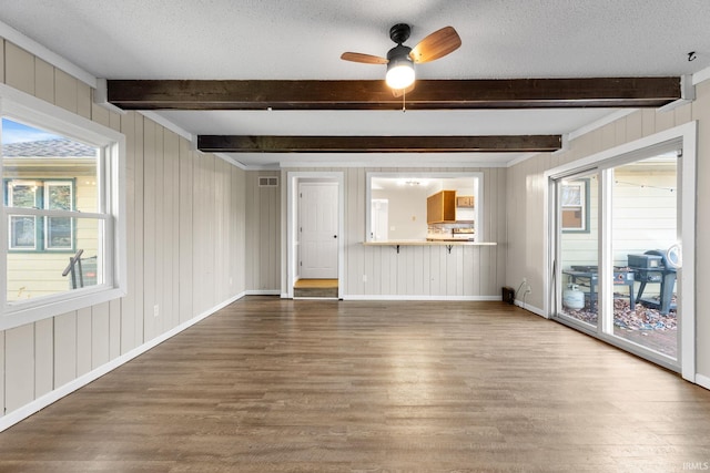 unfurnished living room with beamed ceiling, wood finished floors, and a textured ceiling