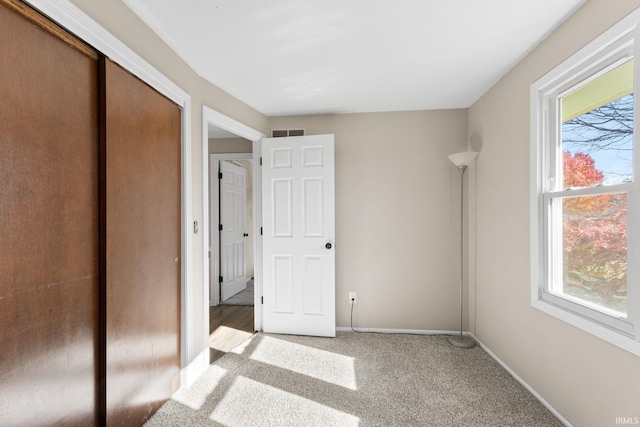 unfurnished bedroom featuring visible vents, multiple windows, light colored carpet, and baseboards