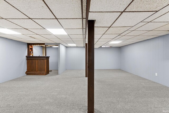 finished basement featuring carpet flooring, a bar, and a paneled ceiling