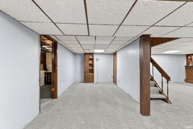 finished below grade area featuring stairway, carpet, wood walls, and a paneled ceiling