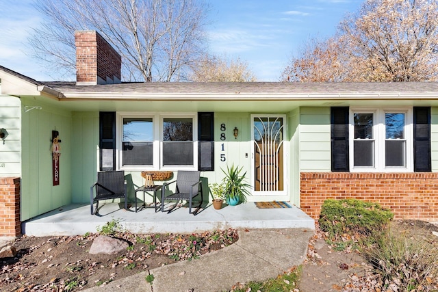 doorway to property featuring brick siding, covered porch, and a chimney