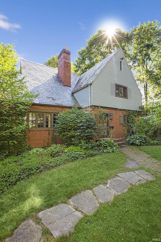 back of house featuring brick siding, a high end roof, a chimney, and a yard