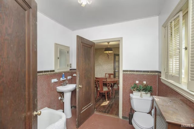 bathroom with a sink, tile walls, toilet, and wainscoting