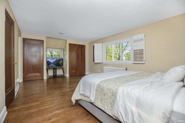 bedroom with radiator heating unit, baseboards, and wood finished floors