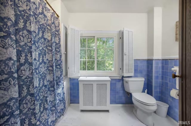 bathroom featuring a shower with shower curtain, radiator, a wainscoted wall, tile walls, and toilet