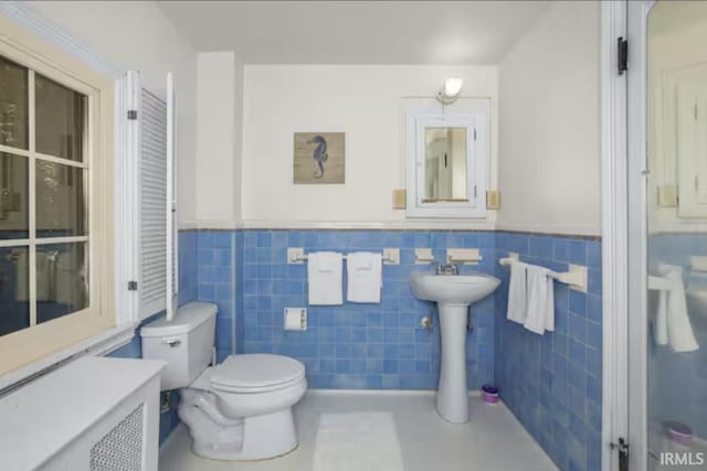 bathroom featuring a sink, tile walls, toilet, and wainscoting