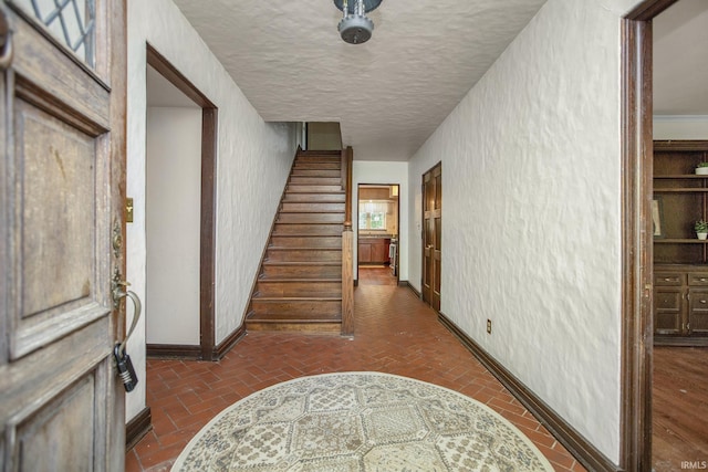 hallway featuring stairway, baseboards, brick floor, and a textured ceiling