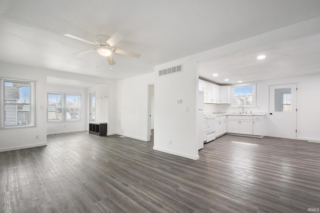 unfurnished living room with a sink, visible vents, baseboards, and dark wood-type flooring