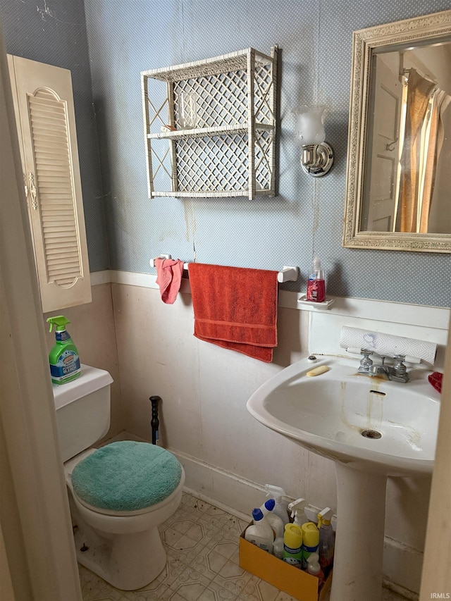 bathroom with wallpapered walls, toilet, and a sink