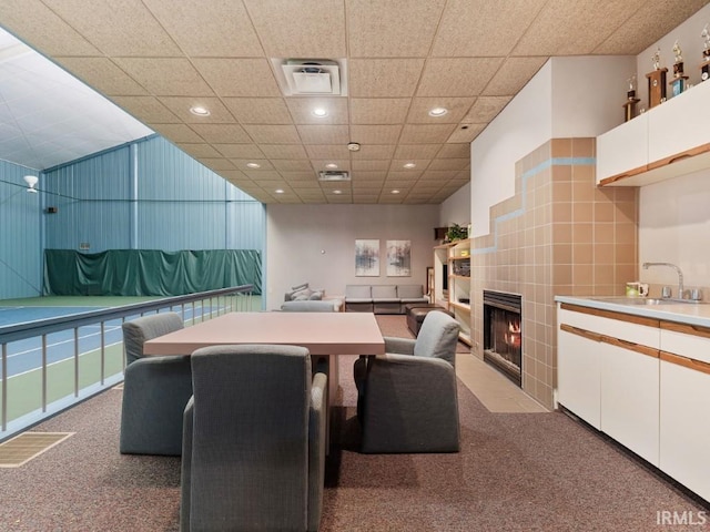 carpeted dining area featuring visible vents, recessed lighting, a drop ceiling, a sink, and a tiled fireplace