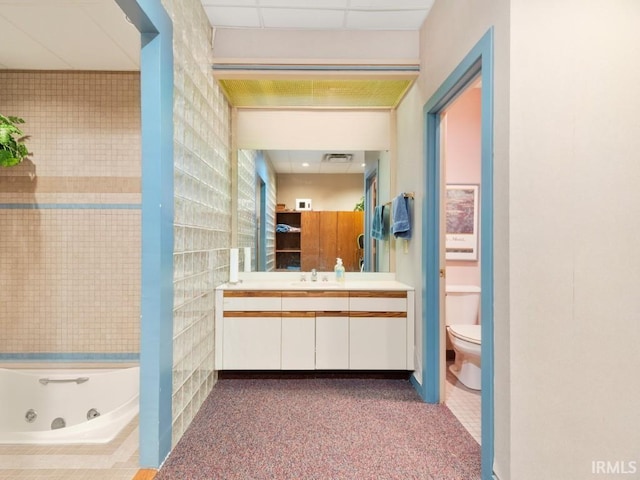 bathroom with visible vents, toilet, a jetted tub, a paneled ceiling, and vanity