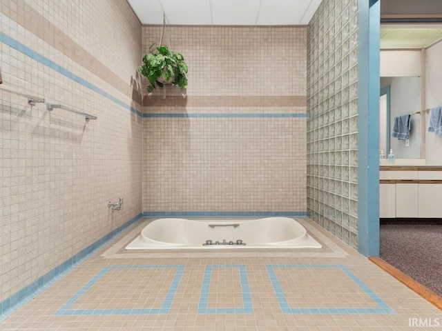 full bathroom with vanity, tile walls, and tiled bath