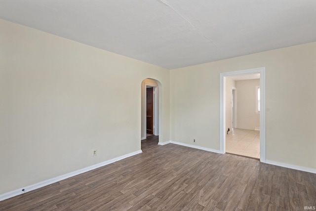 unfurnished room with dark wood finished floors, baseboards, and arched walkways